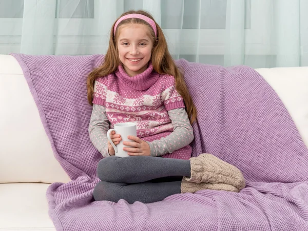 Schönes kleines Mädchen auf einem Sofa mit warmer Decke — Stockfoto