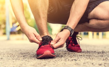 Kırmızı ayakkabılara ayakkabı bağı bağlayan adam.