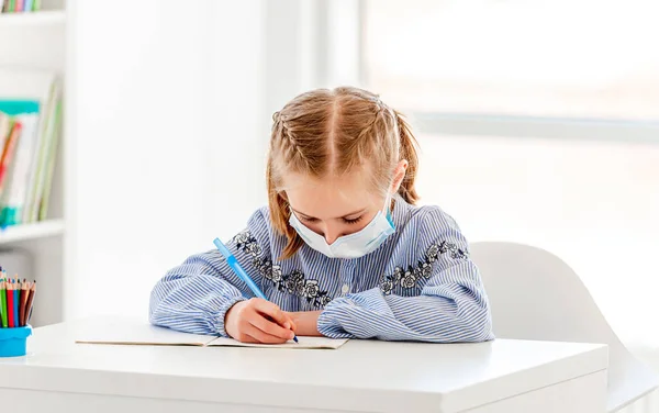 Colegiala en máscara protectora escritura en cuaderno —  Fotos de Stock