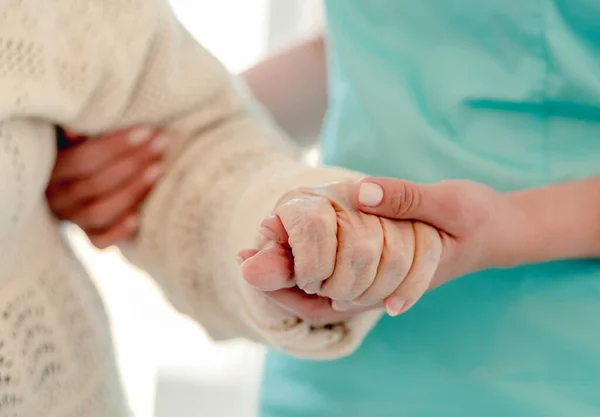 Gammal kvinna lutar sig mot sjuksköterskan medan hon går — Stockfoto