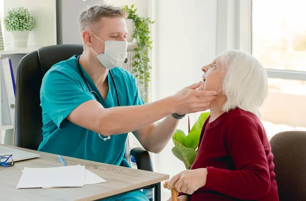 Arzt untersucht Kehle einer alten Frau — Stockfoto