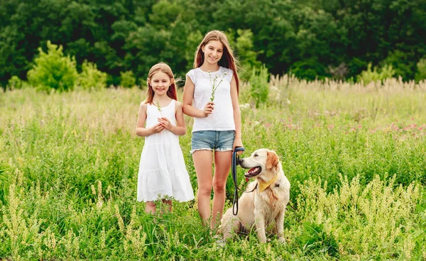 Hermanas con perro en pradera floreciente — Foto de Stock