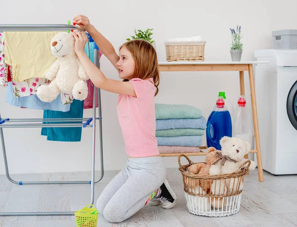 Little girl hanging teddy bear on dryer