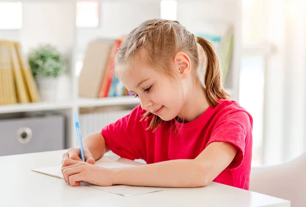 Маленькая девочка пишет в блокноте с ручкой — стоковое фото