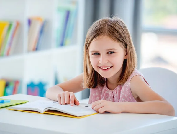 Schoolmeisje met leerboek zit aan het bureau — Stockfoto