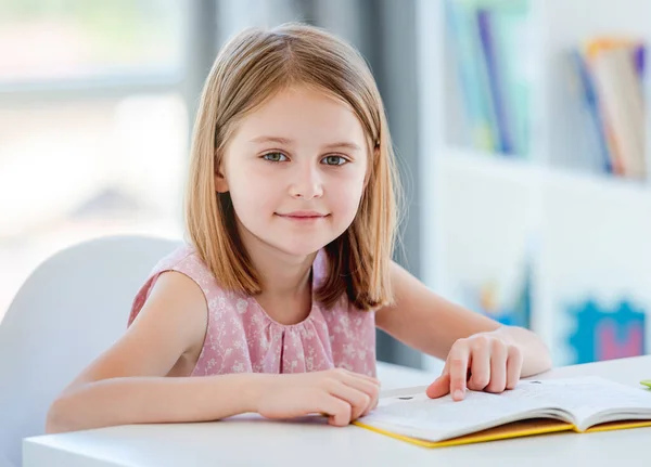 Schulmädchen mit Lehrbuch sitzt am Schreibtisch — Stockfoto