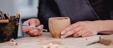 Potter kupa üzerine oyma aracı kullanıyor
