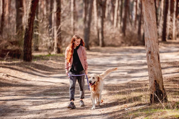 Flicka med golden retriever hund i skogen — Stockfoto