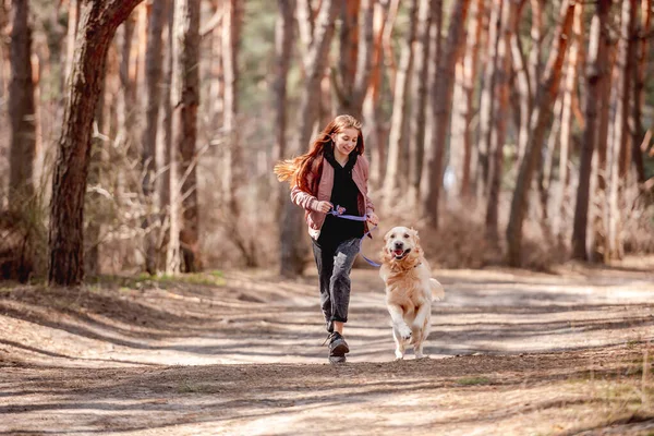 Flicka med golden retriever hund i skogen — Stockfoto