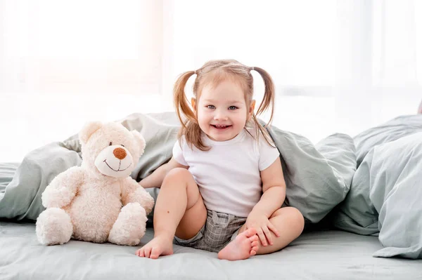 在床上抱着玩具熊的小女孩 — 图库照片