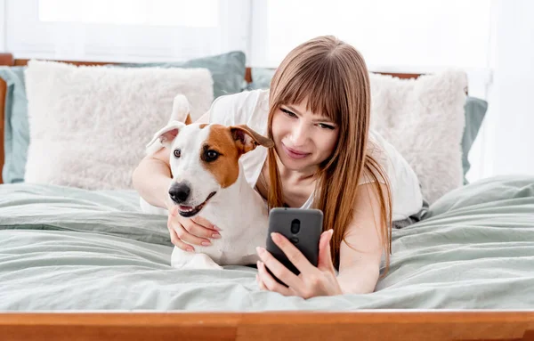 Menina com cão e smartphone na cama — Fotografia de Stock