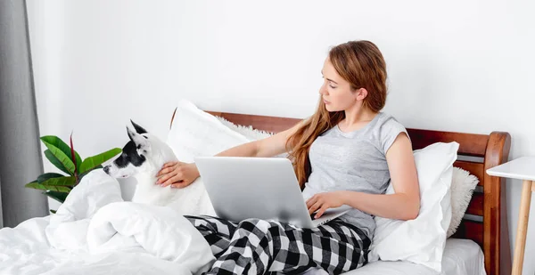 Ragazza con computer portatile e cane nel letto — Foto Stock
