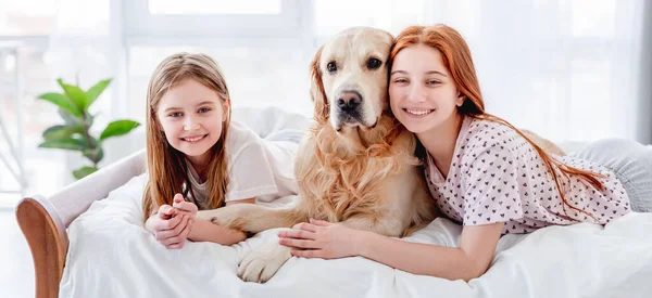 Meisjes met golden retriever hond in het bed — Stockfoto