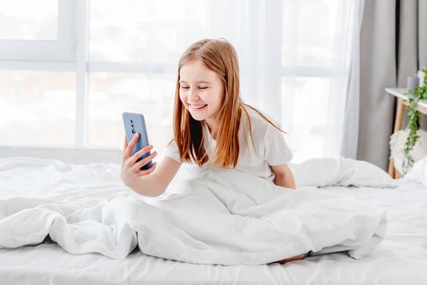 Menina com smartphone na cama — Fotografia de Stock