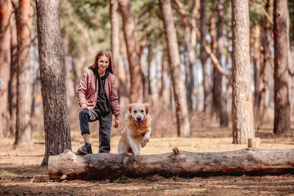 Flicka med golden retriever hund i skogen — Stockfoto