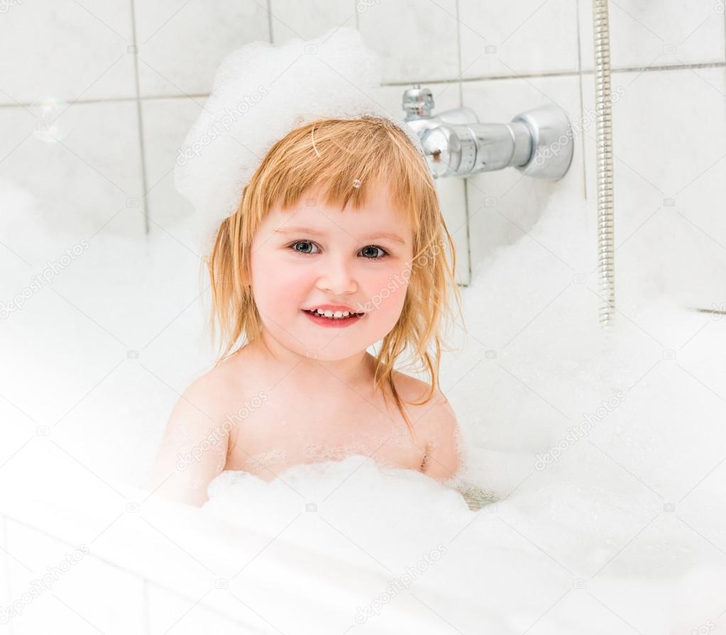 cute two year old baby bathes in a bath with foam