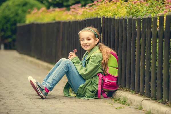 Mooie schoolmeisje zittend op de straat — Stockfoto