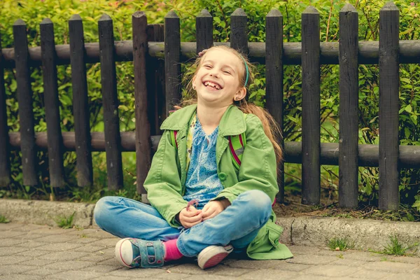 Lachen schoolmeisje zittend op de straat — Stockfoto