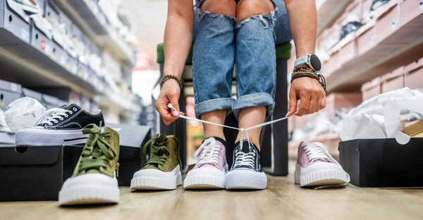 Женщина примеряет кроссовки в разных цветах в магазине обуви