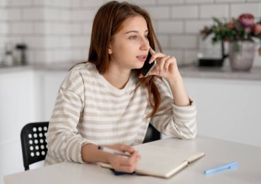 Kız telefonda konuşur ve evdeki deftere yazar.