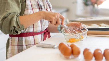 Pişirdiği için yumurta çırpan bir kadının yakın çekimi.