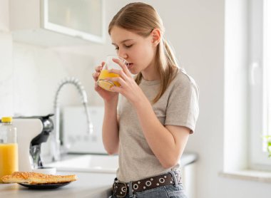 Genç kız, mutfakta kahvaltıda meyve suyu içiyor.