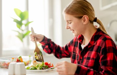 Parlak bir mutfaktaki tabağa sebze koyan gülümseyen kız.