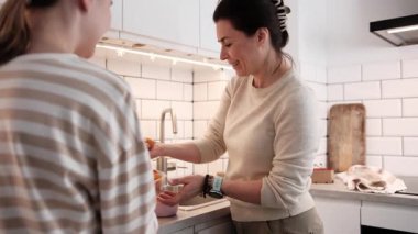 Mutlu küçük kız ve anne evde yemek pişiriyor taze sebzeleri yıkıyor ve birlikte vakit geçiriyorlar.