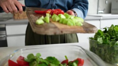 Salatalık ve domates gibi doğranmış sebzeleri salata kasesine dolduran kadın.