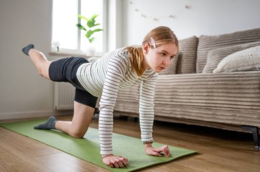 Evde, oturma odasında yoga minderi üzerinde egzersiz yapan bir kız.
