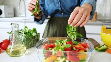 Kadın evdeki mutfakta salata kasesine yeşillik ekliyor.