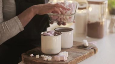 Noel süslemeli bir mutfakta sıcak kakao hazırlayan ve tatmak ve süslemek için şekerlemelerle süsleyen bir kadın.