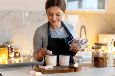 Kadın, Noel süslemeli mutfakta sıcak kakao içkisini kaşıkla karıştırıyor.