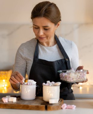 Bir kadın Noel süslemeli mutfakta lokum şekeriyle sıcak kakao hazırlıyor.