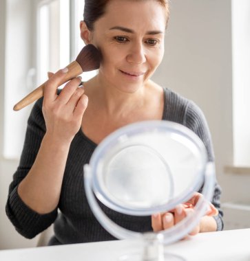 Aynaya bakarken fırçayla pudra süren kadın