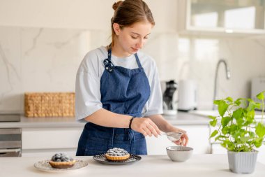 Ev Mutfağında Yaban mersinli böreğin üzerine pudra şekeri serpiştiren kız.