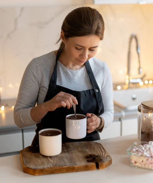 Kadın, Noel süslemeli mutfakta sıcak kakao içkisini kaşıkla karıştırıyor.