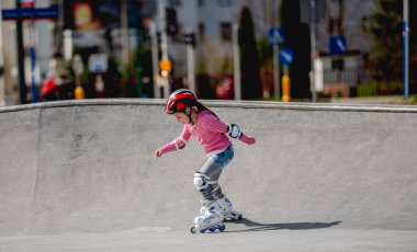 Küçük kız patenle kayıyor İlkbaharda kaskla kayıyor