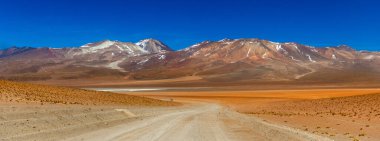 Bolivya 'da Altiplano' daki çöl yolunda. Arka planda tuz düzlükleri ve dağlar var.