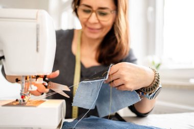 Bir kadın dikiş makinesinde dikiş dikiyor ve ipliği kesiyor.