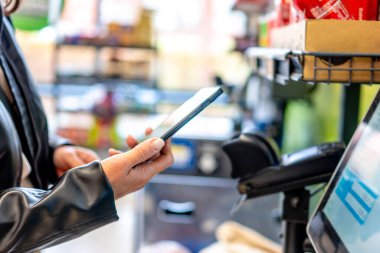 Kadın süpermarkette kendini kontrol ederken telefonunu kullanıyor.