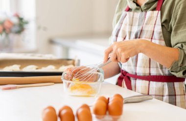 Pişirdiği için yumurta çırpan bir kadının yakın çekimi.