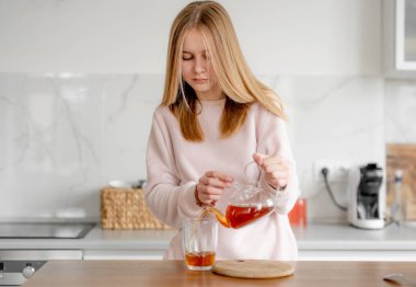 Genç kız evinde fincana çay dolduruyor.