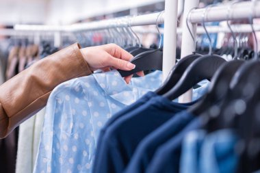 Kadın eli elbise mağazasında bluzla askıyı tutuyor.