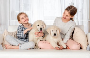 Oturma odasında, kanepesinde altın köpek yavrusu olan iki küçük kız kardeş.