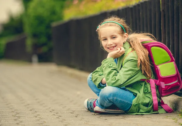 Mooie schoolmeisje zittend op de straat — Stockfoto