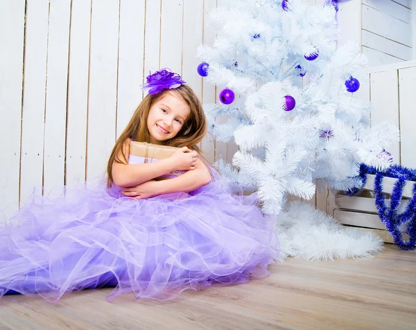 Little girl with a gift   near Christmas tree — Stock Photo, Image