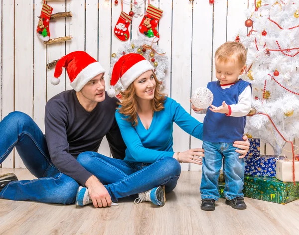 Ung familj i röda hattar med lille son nära julgranen — Stockfoto