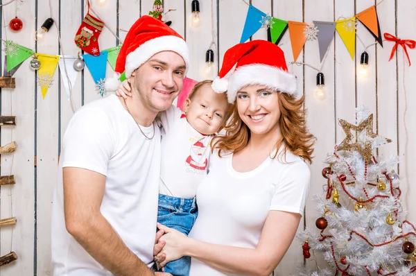 Νεαρή οικογένεια σε κόκκινα καπέλα με το μικρό του γιο κοντά το χριστουγεννιάτικο δέντρο — Φωτογραφία Αρχείου