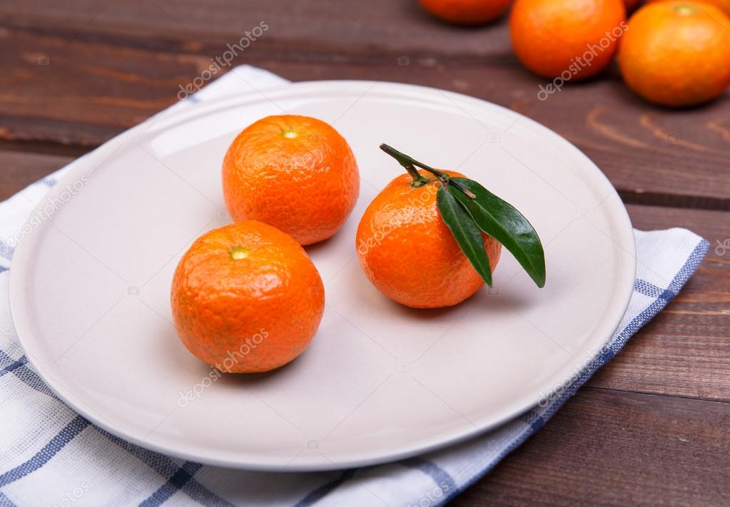 three tangerines on a plate on a wooden table — 图库照片